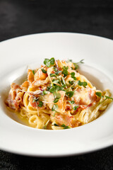 Classic carbonara pasta with a creamy sauce and garnished with fresh herbs, presented on a white plate