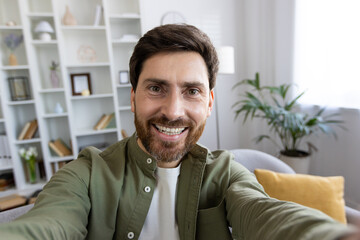 First person view of happy caucasian male in shirt recording video on digital camera. Popular influencer producing content fro new post in social median and new post in personal blog from home.