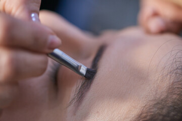 Close-up shot of a young caucasian Latin lady having her eyebrows defined by a professional makeup...