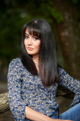 Fototapeta premium A confident, stylish woman in jeans and blue blouse poses casually in a sunny park, exuding modern urban elegance