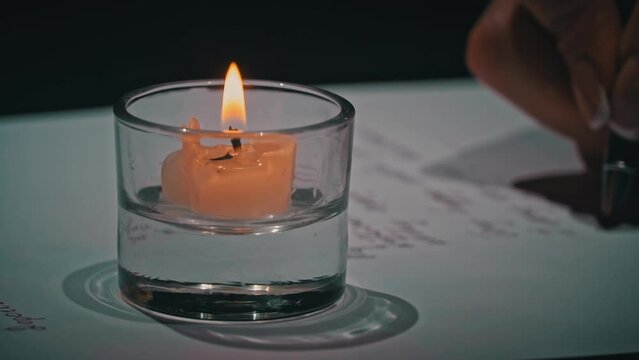 Man's hand writes with an antique pen on white paper close-up. Writes a calligraphy letter using a vintage pen and ink on a sheet of white paper. Write a letter in capital letters by candlelight.
