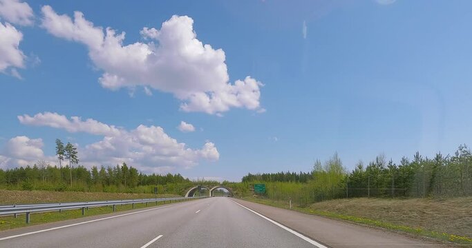 POV driving on highway E18 into a small tunnel and under a bridge in spring with clouds, Pyhtää, Finland.