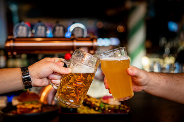Two friends hands clinking glasses of craft beer at the pub or bar
