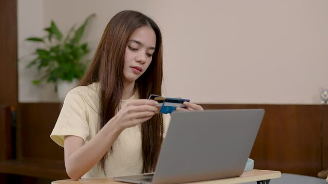 Asian lady with laptop, comparing credit cards, online shopping, decision-making at home. Thoughtful woman analyzing credit cards, engaging in e-commerce, serious financial consideration