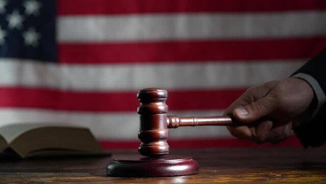Judge's hand with wooden judge gavel and soundboard on the American flag background, close up