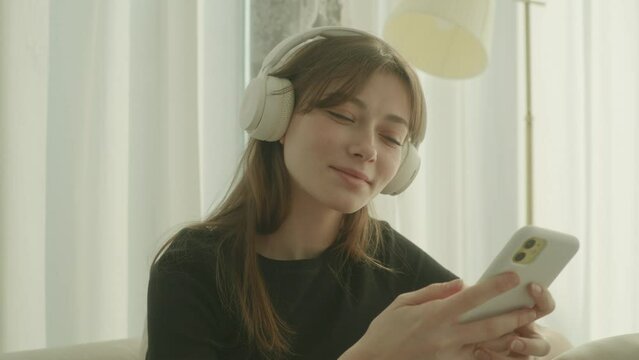 A young woman listening to music through her phone and headphones, and happily grooving. daytime, indoors. 
