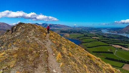 backpacker walking alongside a ridge and admiring the panorama of southern alps from the summit of...