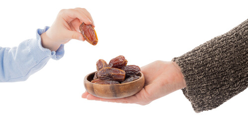 Ramadan concept idea, woman holding wooden plate full of date fruits. Child hand taking one of the...