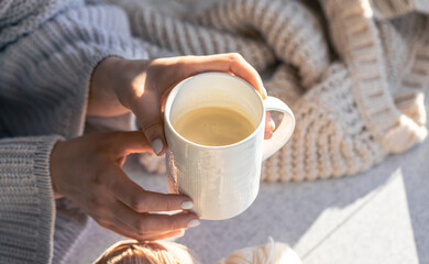 A cup of coffee in female hands on a blurred background with a knitted element.