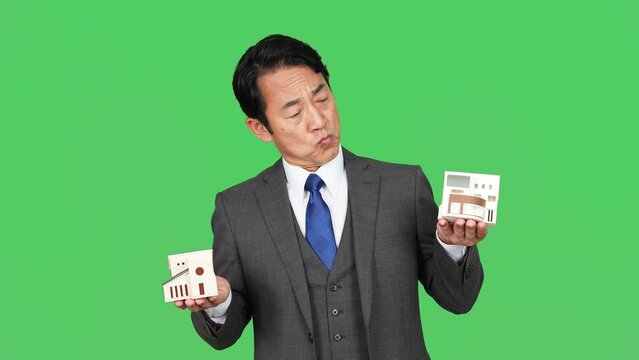住宅模型を持って悩む中年ビジネスマン　クロマキー合成用グリーンバック