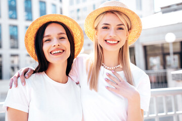 Two young beautiful smiling hipster female in trendy summer white t-shirt and jeans clothes. Carefree women posing in street. Positive models having fun. Cheerful and happy. In hat