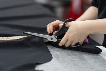 female tailor cutting fabric with scissors in the office