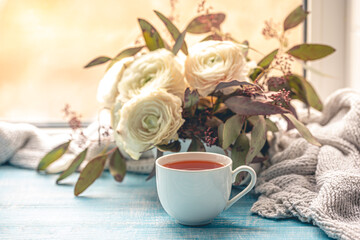 Composition with a cup of tea, flowers and a knitted element.