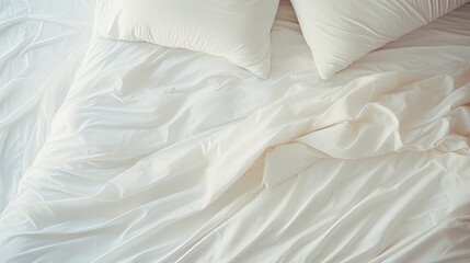 Top view of a crumpled white bed with a sheet, blanket, pillows in the light and shade from the window early in the morning.