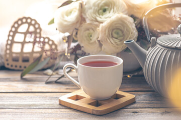 Cozy home composition with a cup of tea, teapot and flowers.