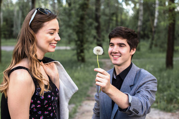 Fototapeta premium Portrait of young couple in love blowing dandelion in the park