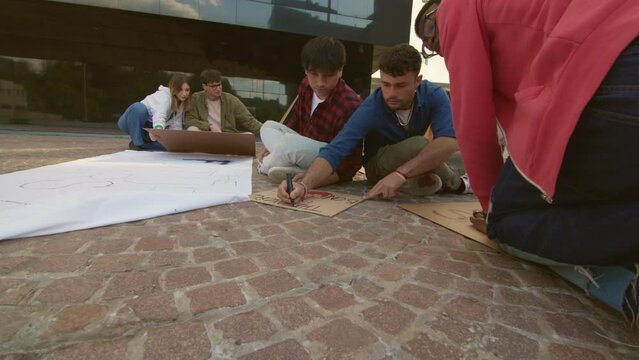 young people sitting on the street together, preparing signs for the climate change march