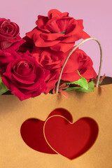 Red roses inside the brown paper shopping bag with two red hearts printed on the gift bag on a pink background