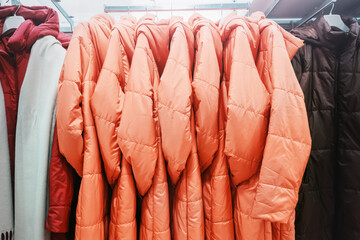 Orange synthetic warm winter women's coats or jackets hanging in a row on hangers in store