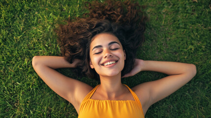 Naklejka na ściany i meble young woman lying on grass, smiling with her eyes closed, and her arms resting behind her head, clearly enjoying a moment of relaxation outdoors.