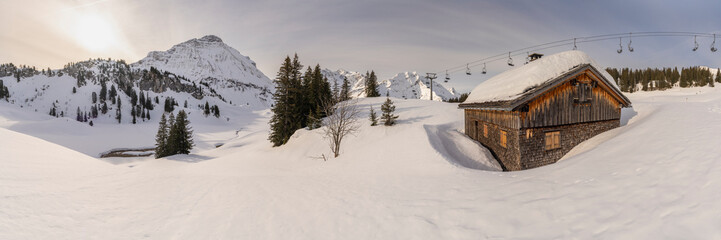 Panorama view with wooden holiday house on edge of forest in snowy mountains in Bregenzerwald,...