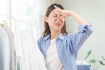 Asian young housewife woman having bad smelling clothes hand holding breath nose with finger, sniff smelly dirty stinky musty, look disgusting from clothes after washed, laundry out of machine at home