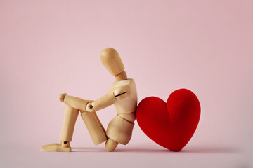 Wooden mannequin sitting with heart on pink background - Concept of love