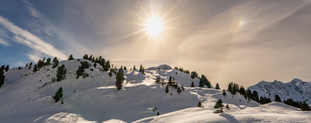 sun star behind veil cloud with halo over shadow valley with illuminated snowy mountains in background. on the road again through Bregenz forest and Austrians mountains. impressive mood