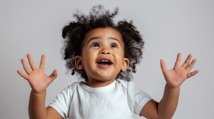 joyful toddler with pigtails is raising her hands in excitement and looking up, set against a plain light background