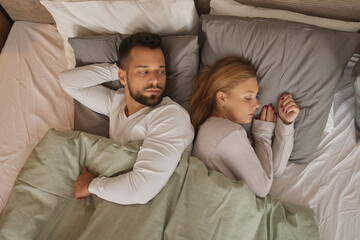 Fototapeta na wymiar Displeased couple lying back to back on a bed and ignoring each other