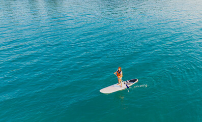 Happy Asian young woman  standing on a sup Surfing balancing on supboard paddling with water sea background
