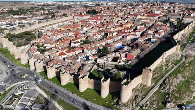 Rising scramble flight viewing the medieval walled city of Avila UNESCO World Heritage Site seeing its houses inside the wall and a road with cars  in circulation on a sunny winter day in Spain