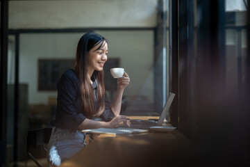 A serene businesswoman sipping coffee while engaging with her laptop in a bright and modern...
