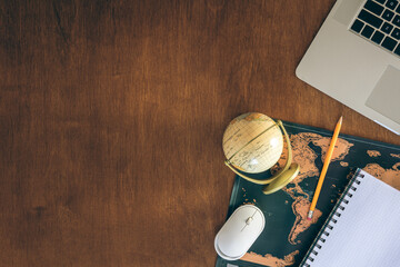 Laptop, map, globe and notepad on a wooden table, top view.