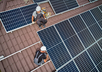Men workers installing photovoltaic solar moduls on roof of house. Engineers in helmet building...
