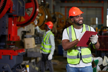 African factory worker or engineer writing on clipboard beside machine in the factory