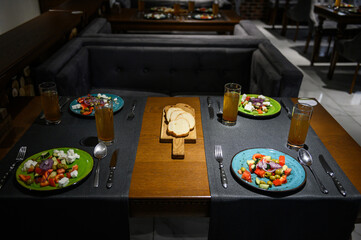 Obraz na płótnie Canvas Greek salad. A set table with cutlery for four people in a restaurant. Fresh greek salad with tomato, cucumber, bell pepper, olives, and feta cheese on blue plate, top view, dark table.