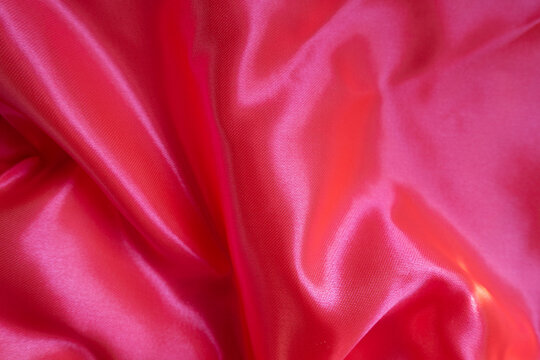 Vibrant reddish pink satin polyester fabric in soft folds
