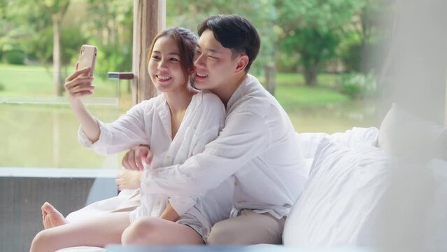 Asia people young adult man woman relax smile look camera take photo post to social media vlog video at outdoor hotel balcony enjoy date day. Happy asian lover wife husband just married sweet newlywed