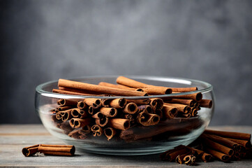 Cinnamon sticks in glass plate on wood board at grey textured wall, rustic style. Still life natural food of ceylon cinnamon sticks on wooden table. Delicious tasty healthy concept. Copy ad text space - obrazy, fototapety, plakaty