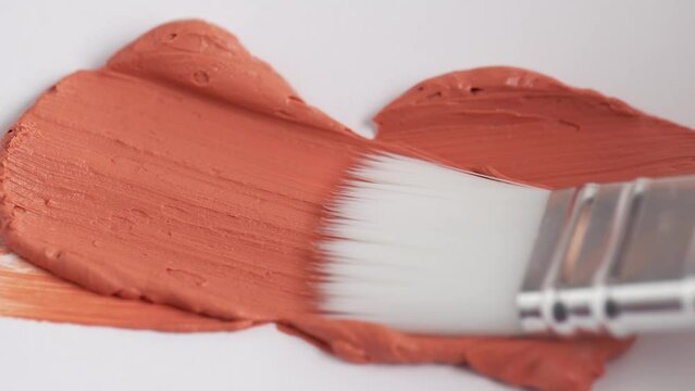 Texture of orange clay mask. Swatch of red clay mask. Makeup brush applying orange facial mask on white background.