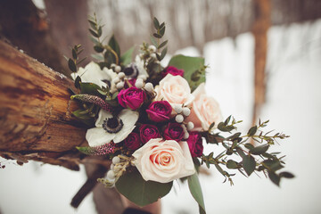 Pink and purple roses with eucalyptus bouquet on a wood log in the snow.