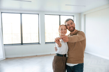 Happy couple as new owners of the house holding the keys in hands