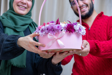 As a surprise in their home, a happy Muslim male gives roses to his mother