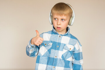 Little boy with headphones listening to music and showing thumbs up on gray background