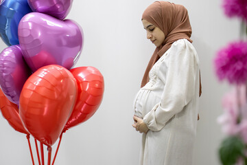 pregnant Arabic muslim female on isolated white background touching her tummy showing her body...