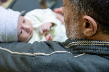 Grandfather holding baby with smile on his face, grey beard , baby holding finger