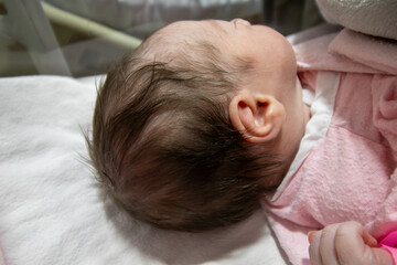 On her first day of life, a newborn baby girl wears a pink hospital ID bracelet on her hand