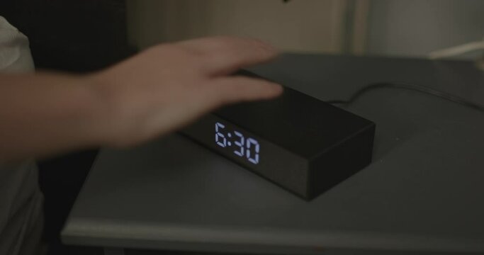 Alarm clock turns to 6:30 in the morning, a woman taps the clock and snoozes the alarm