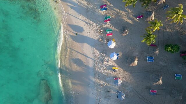 Aerial static view of crystal clear water in Curacao and multicolored chairs with palm tree shadows